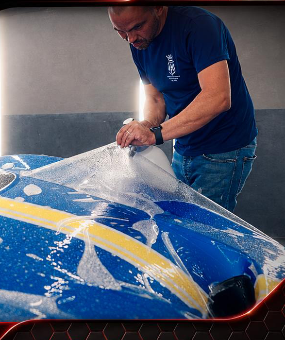 MA-FRA technician applying Forever Young PPF to a blue race car bonnet with slip solution for precise alignment